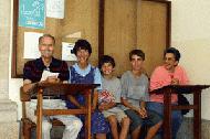 Amadeu, Therese, Paul, Peter and Helen sit in the hallway of Amadeu's high school 65 years later.